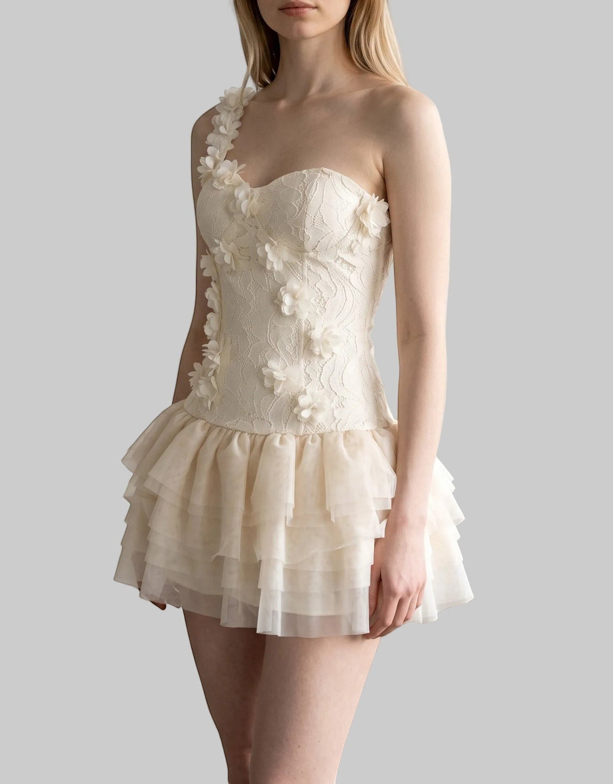 Cream one-shoulder corset mini dress with 3D rose appliqués, floral lace, and layered mesh ruffle skirt.