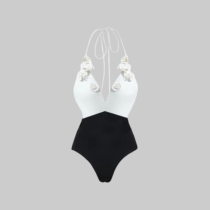 LUNRIA black and white halter one-piece swimsuit featuring floral appliqué details, a plunging V-neckline, high-waisted color-block design, and strappy open back.