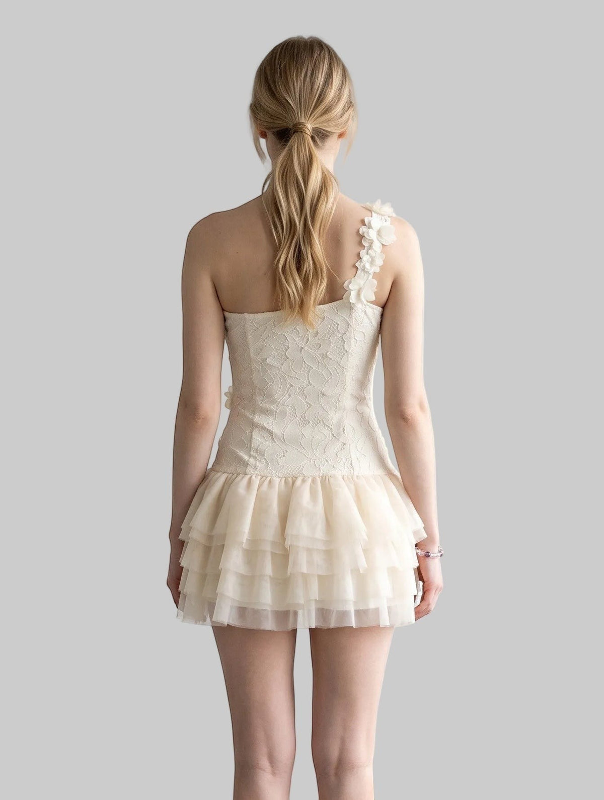 Cream one-shoulder corset mini dress with 3D rose appliqués, floral lace, and layered mesh ruffle skirt.