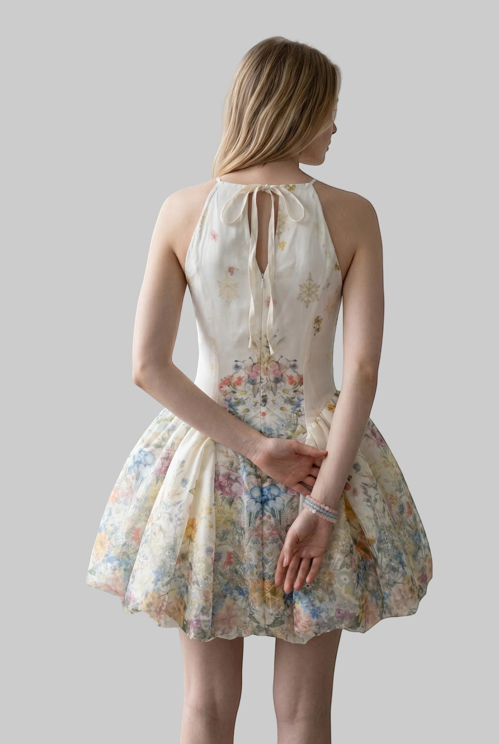 LUNRIA floral watercolor halter mini dress featuring a soft multicolor floral print, fitted bodice, open tie-back detail, and voluminous bubble skirt.