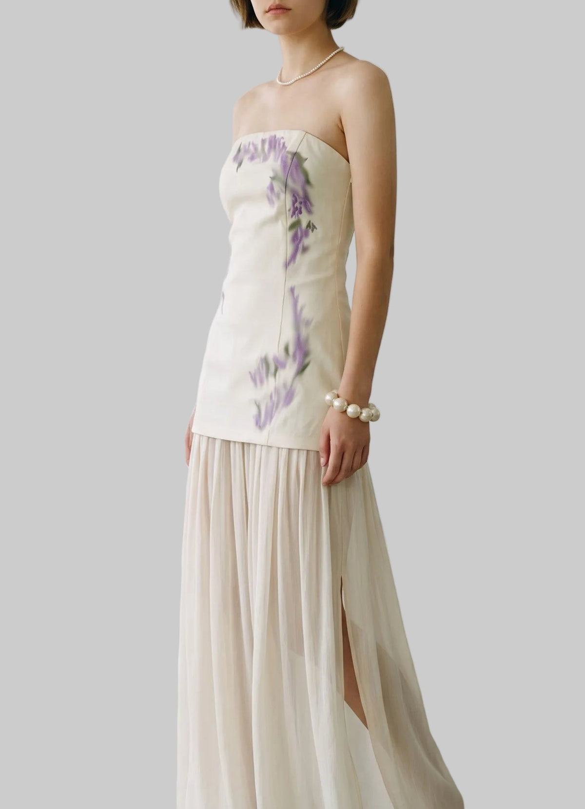 Ivory strapless maxi dress with lavender floral print, fitted bodice, and flowing pleated chiffon skirt.