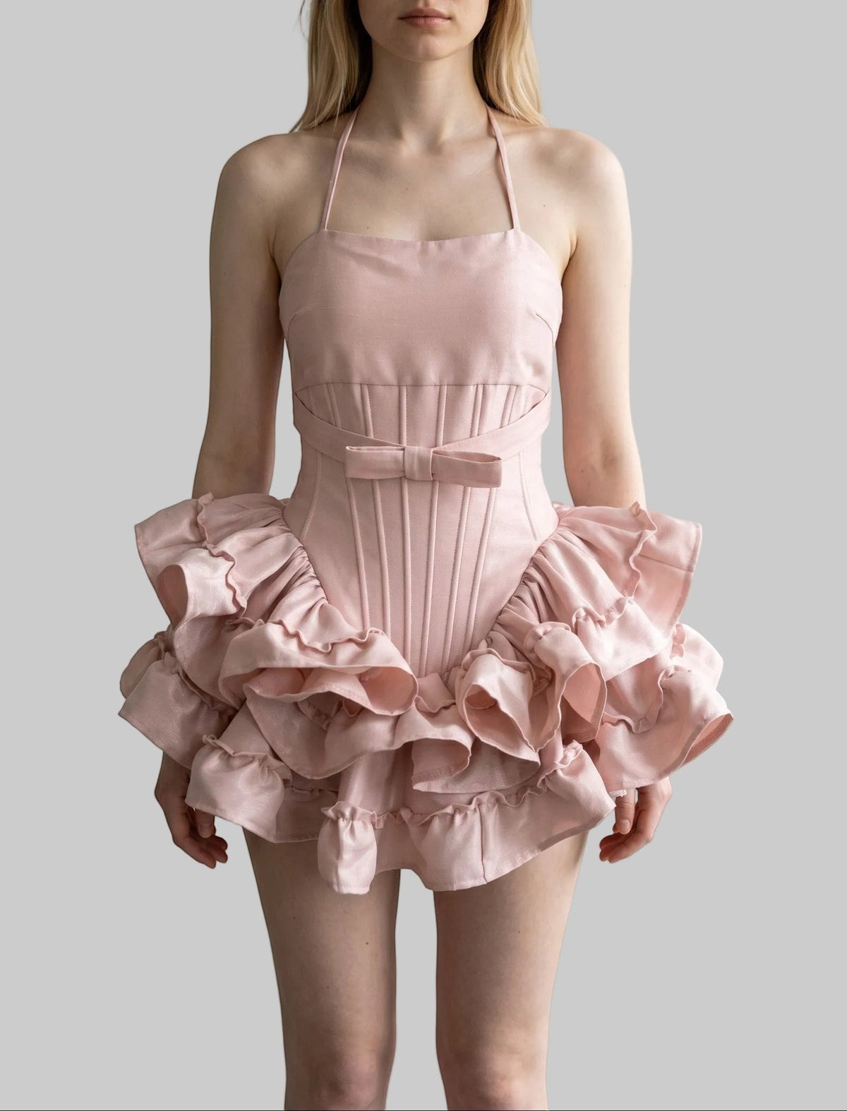 Blush pink halter corset mini dress with bow detail, structured waist, lace-up back, and layered ruffle skirt.