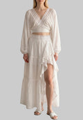 White two-piece set with a balloon sleeve wrap crop top, lace trim, and an asymmetrical ruffle maxi skirt.